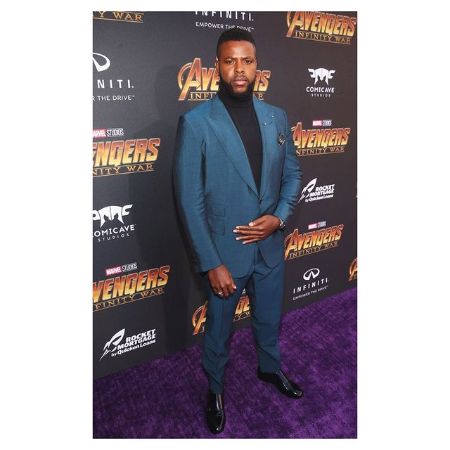 Winston Duke in a suit strikes a pose for the photo.